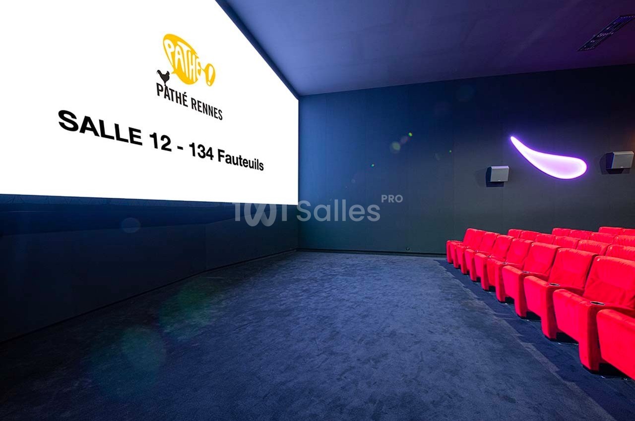 Salle de cinéma moderne avec écran allumé, rangées de sièges rouges et mur sombre.