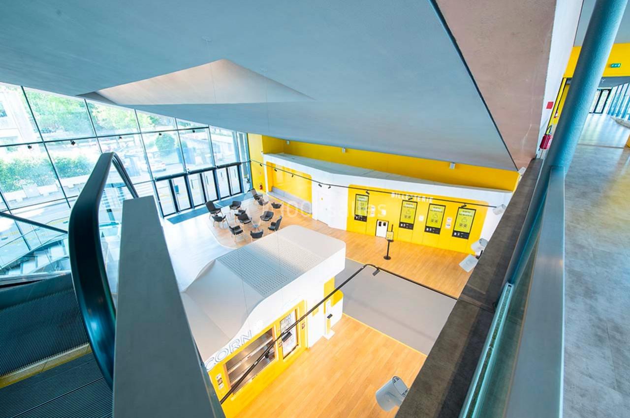 Vue intérieure d'un espace moderne avec escalier, bornes interactives jaunes et mobilier dans un hall lumineux.