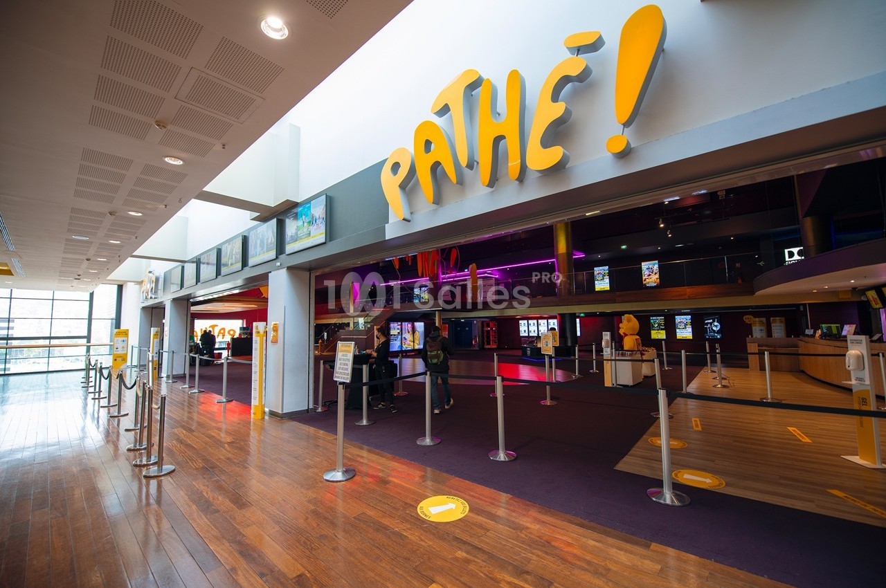 Entrée d'un cinéma avec le logo ’Pathé’, des bornes automatiques et des files d'attente délimitées par des poteaux.