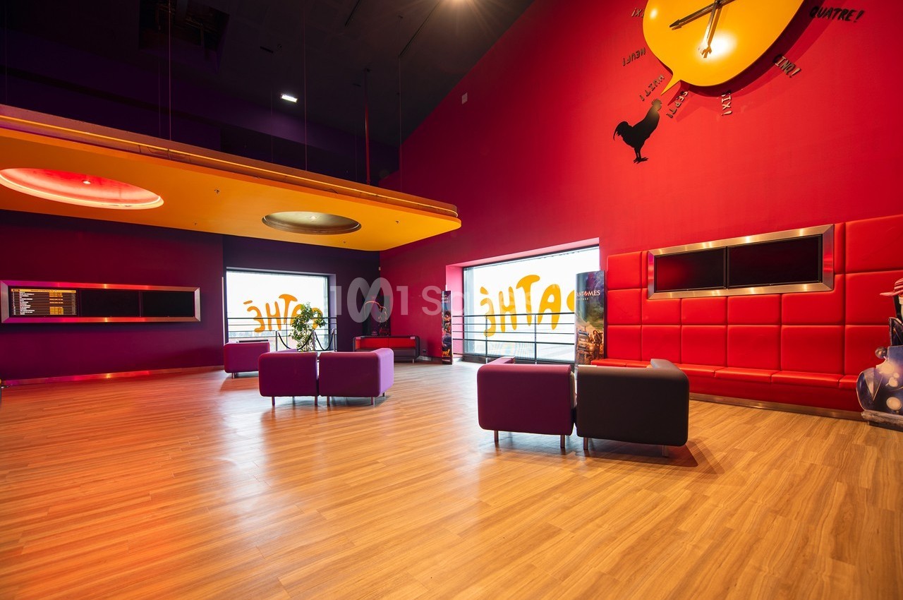 Salle moderne avec murs rouges, mobilier coloré, sol en bois clair et grande horloge murale décorative.