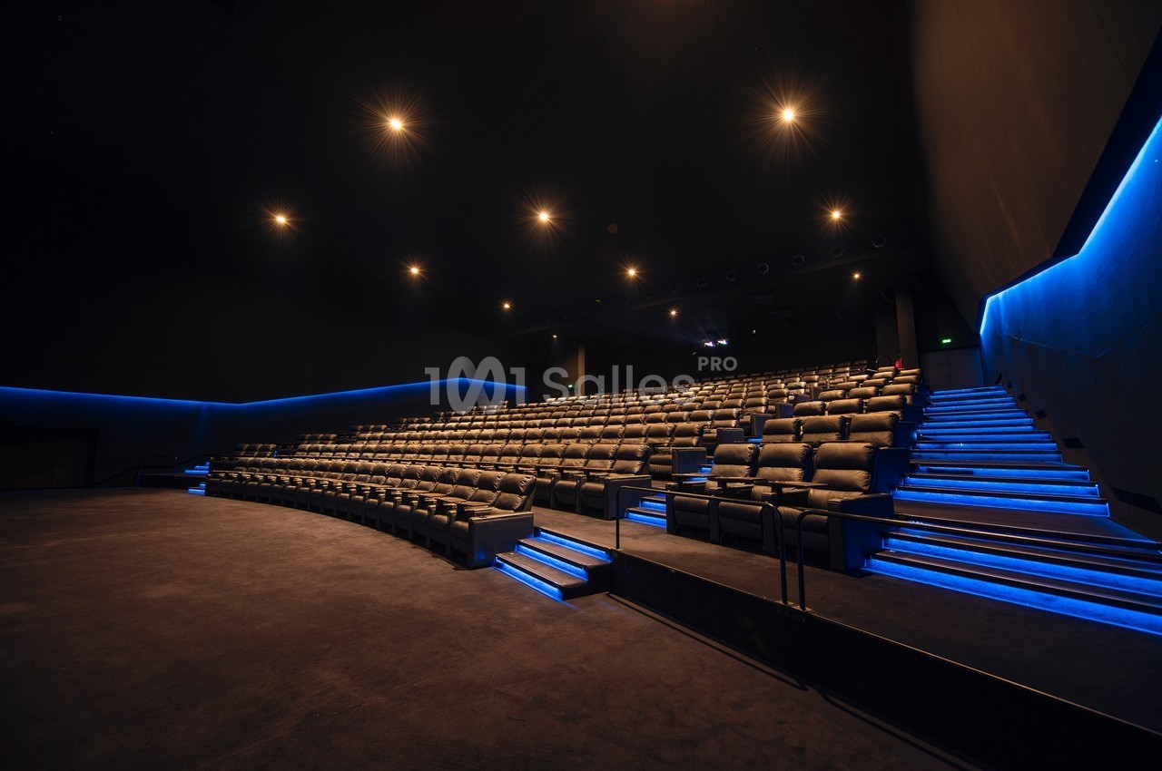 Salle de cinéma vide avec rangées de sièges en cuir et éclairage bleu le long des allées.