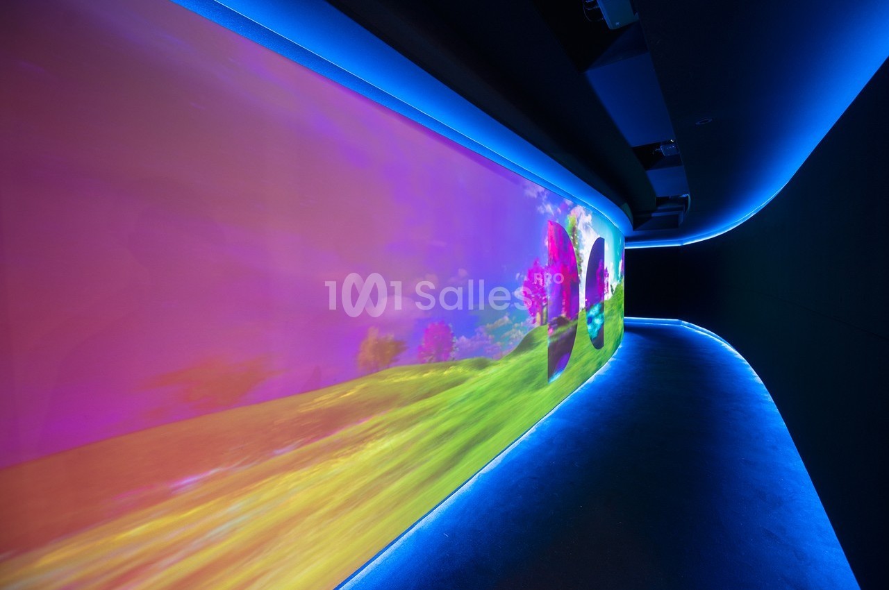 Projection colorée d'un paysage lumineux avec des arbres roses sur un mur incurvé dans un espace sombre.