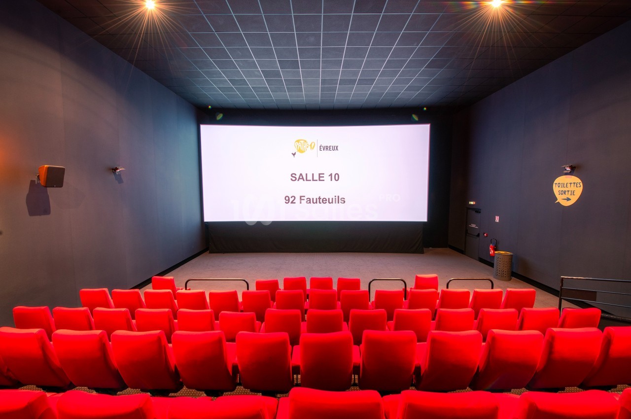 Salle de cinéma vide avec 92 fauteuils rouges, écran blanc affichant ’Salle 10’, éclairage tamisé.