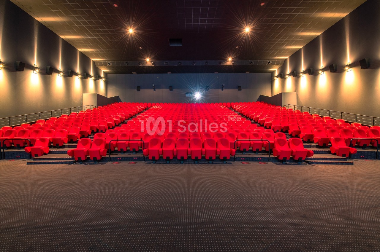 Salle de cinéma vide avec des rangées de sièges rouges et un écran illuminé en arrière-plan.