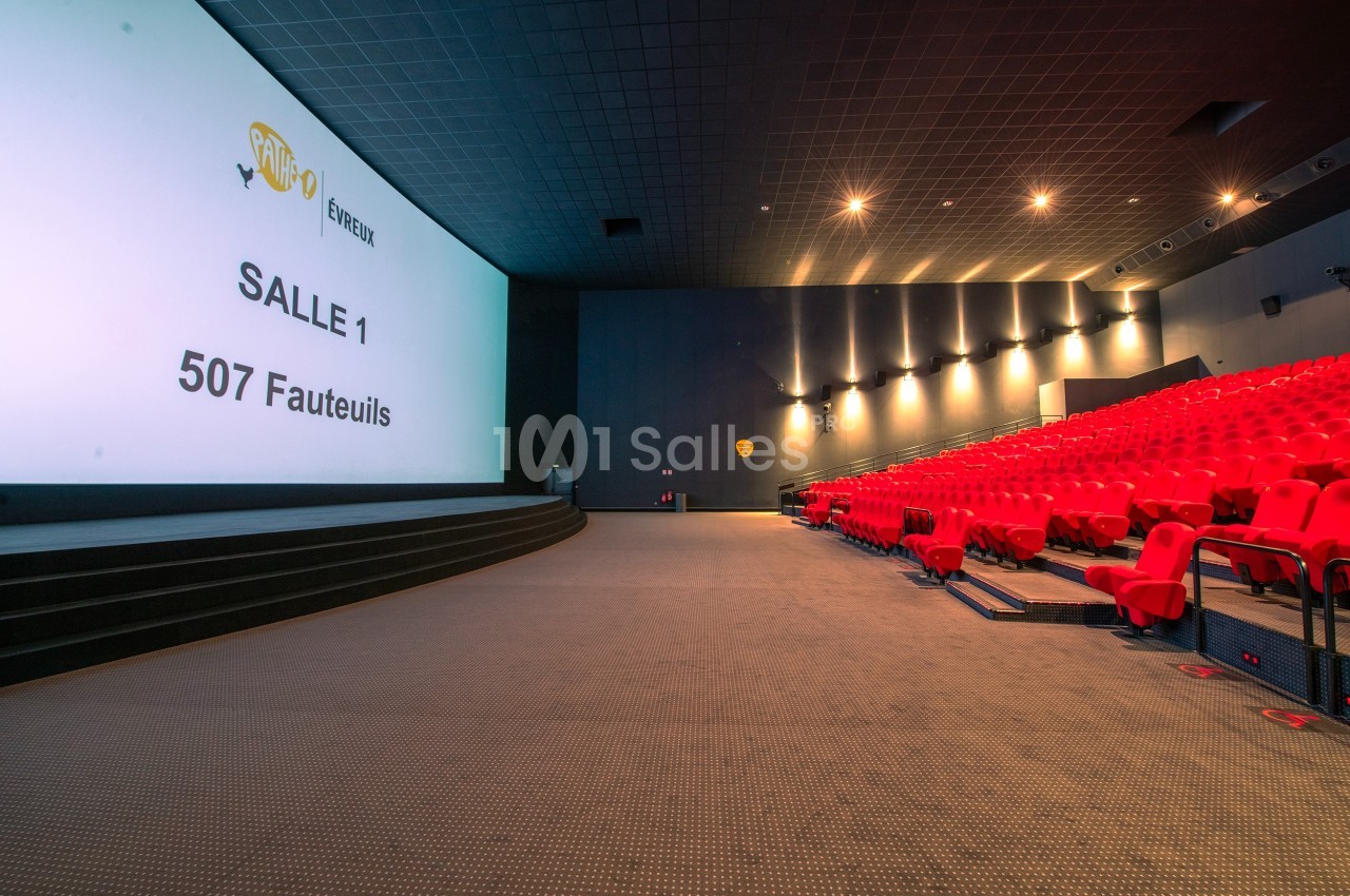 Salle de cinéma avec écran géant, rangées de fauteuils rouges et éclairage tamisé.