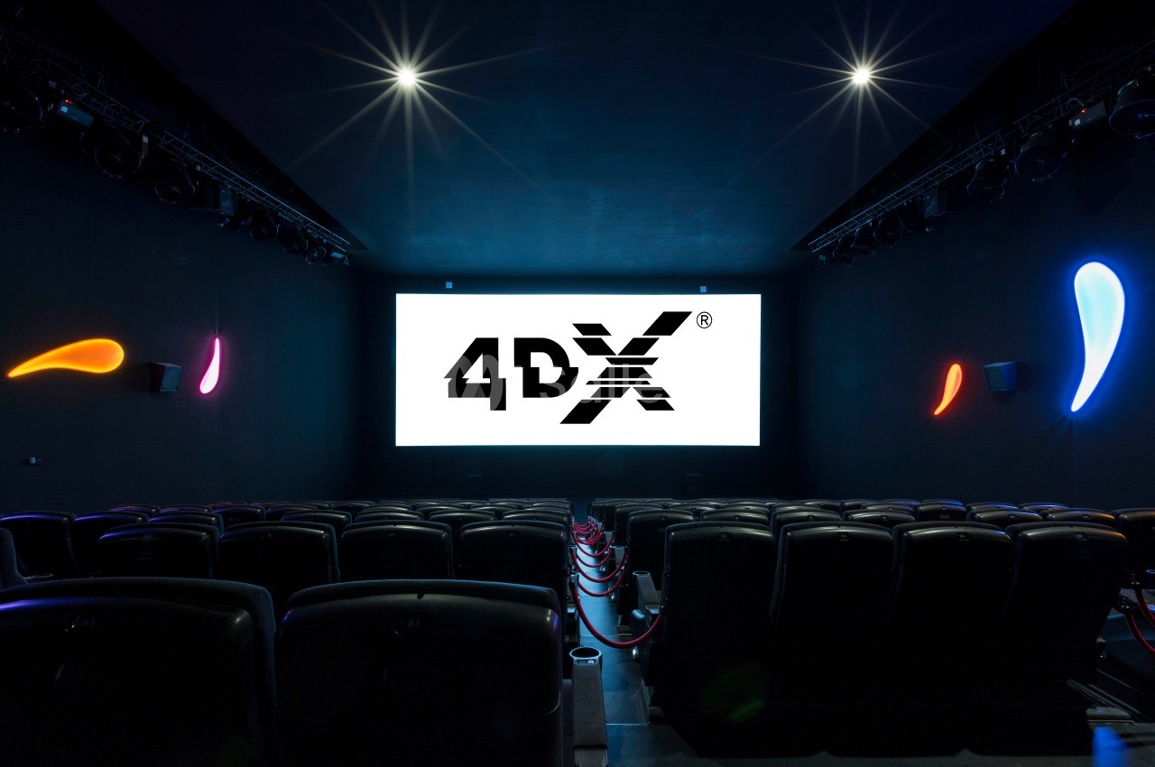 Salle de cinéma 4DX vide avec écran allumé, sièges noirs et éclairage coloré sur les murs.