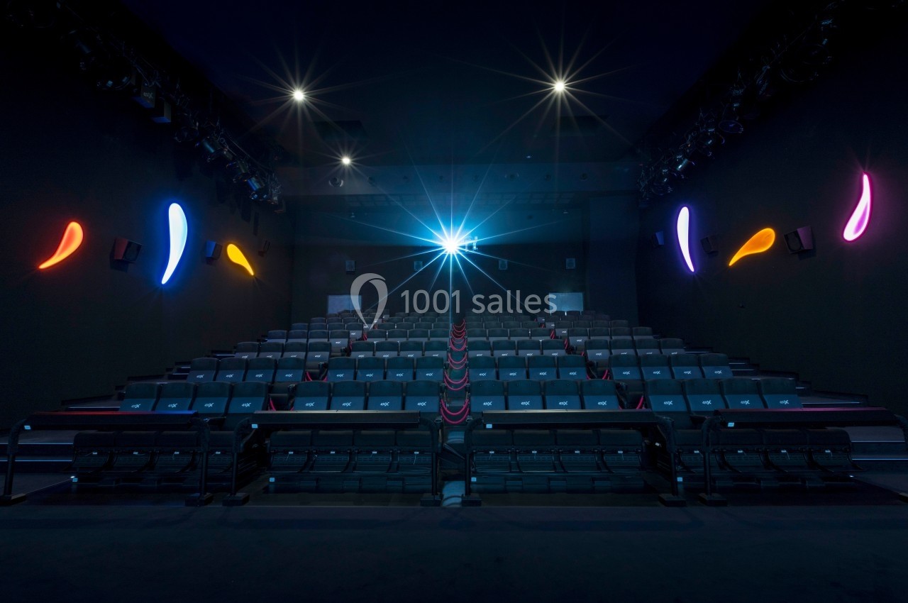 Salle de cinéma vide avec rangées de sièges alignés et éclairage coloré sur les murs sombres.