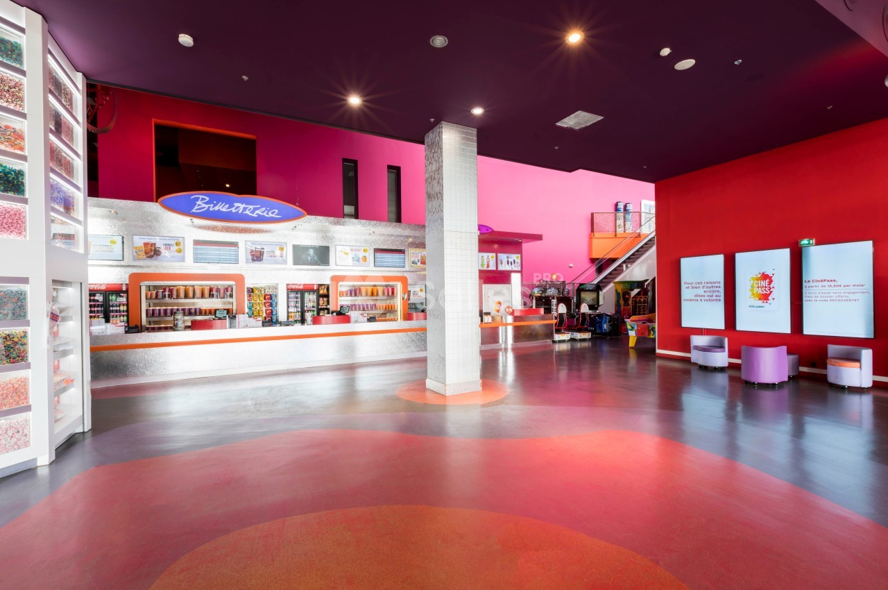 Intérieur d'un espace coloré avec un comptoir de confiseries, des étagères remplies de bonbons et un escalier au fond.