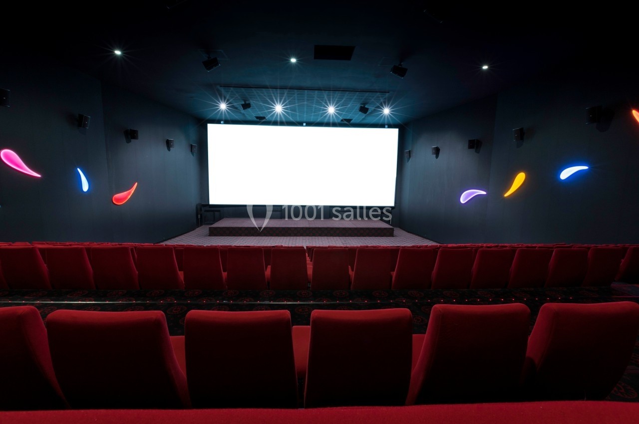Salle de cinéma vide avec écran blanc allumé, sièges rouges et éclairages muraux colorés.