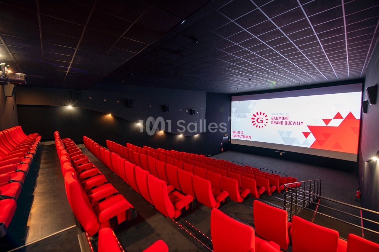 Salle de cinéma vide avec des rangées de fauteuils rouges et un écran affichant une présentation.