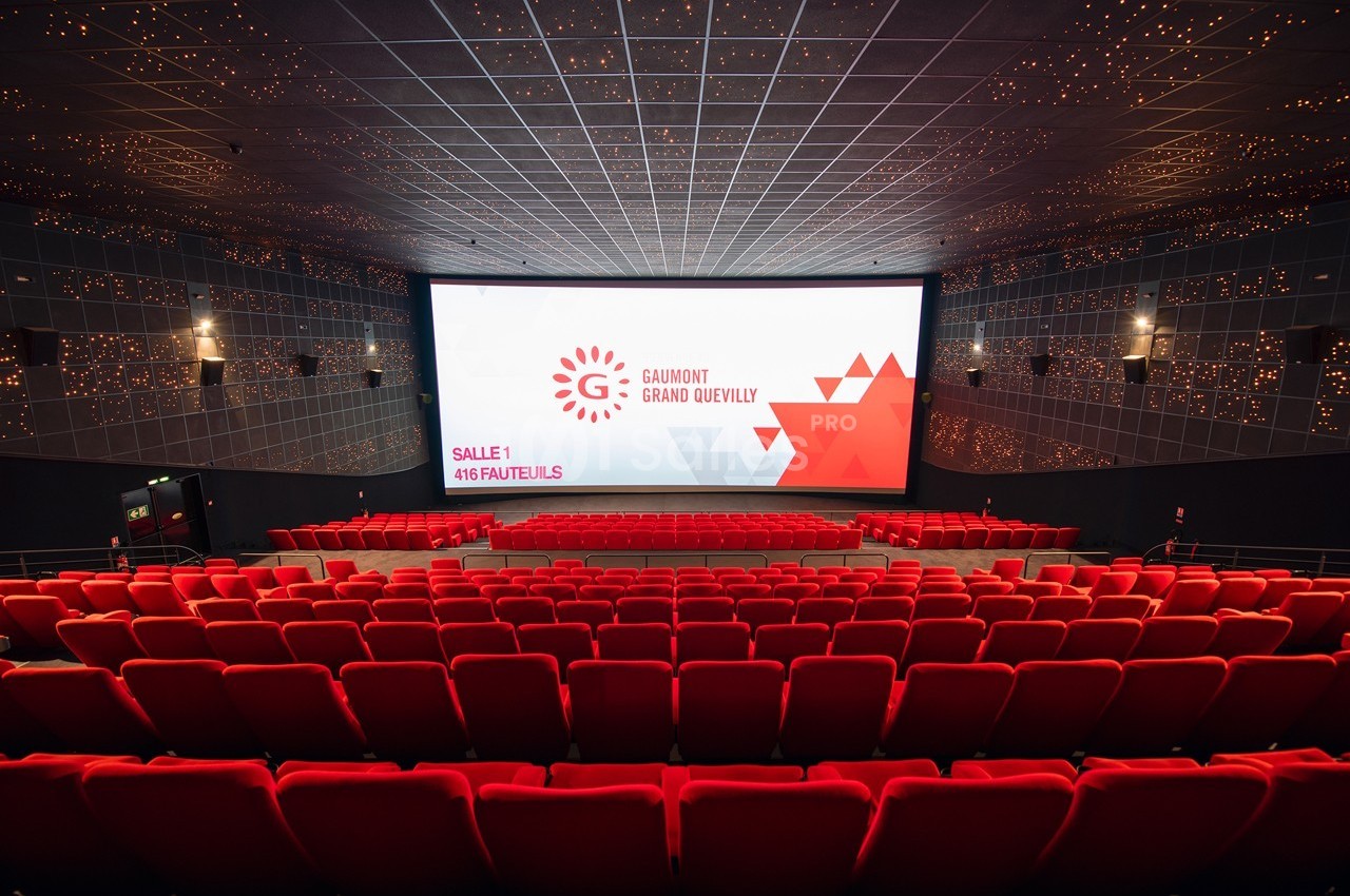 Salle de cinéma vide avec rangées de fauteuils rouges, grand écran affichant ’Gaumont Grand Quevilly, Salle 1, 416 fauteuils…
