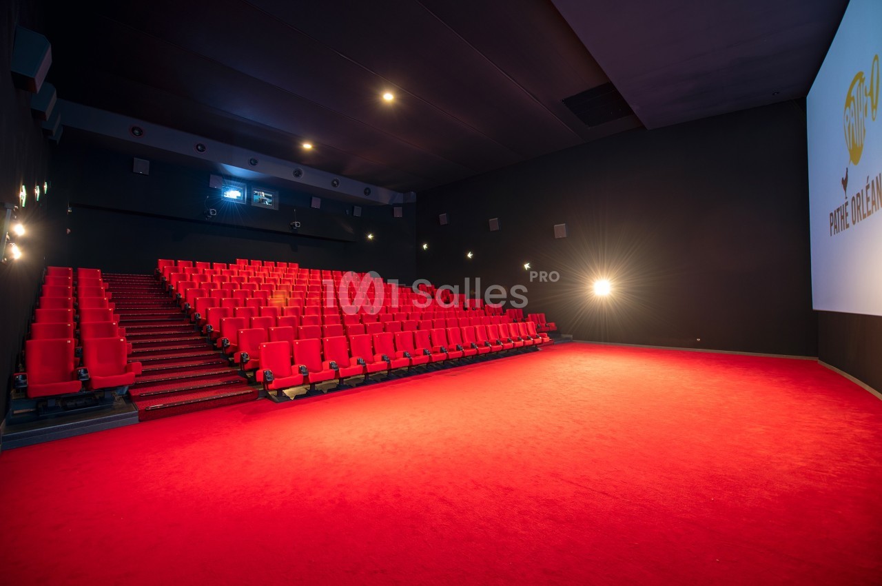 Salle de cinéma vide avec sièges rouges, écran blanc et éclairage tamisé.