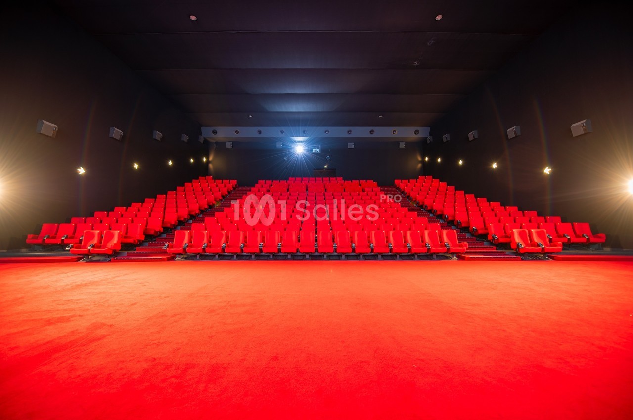 Salle de cinéma vide avec des rangées de sièges rouges et un éclairage tamisé.