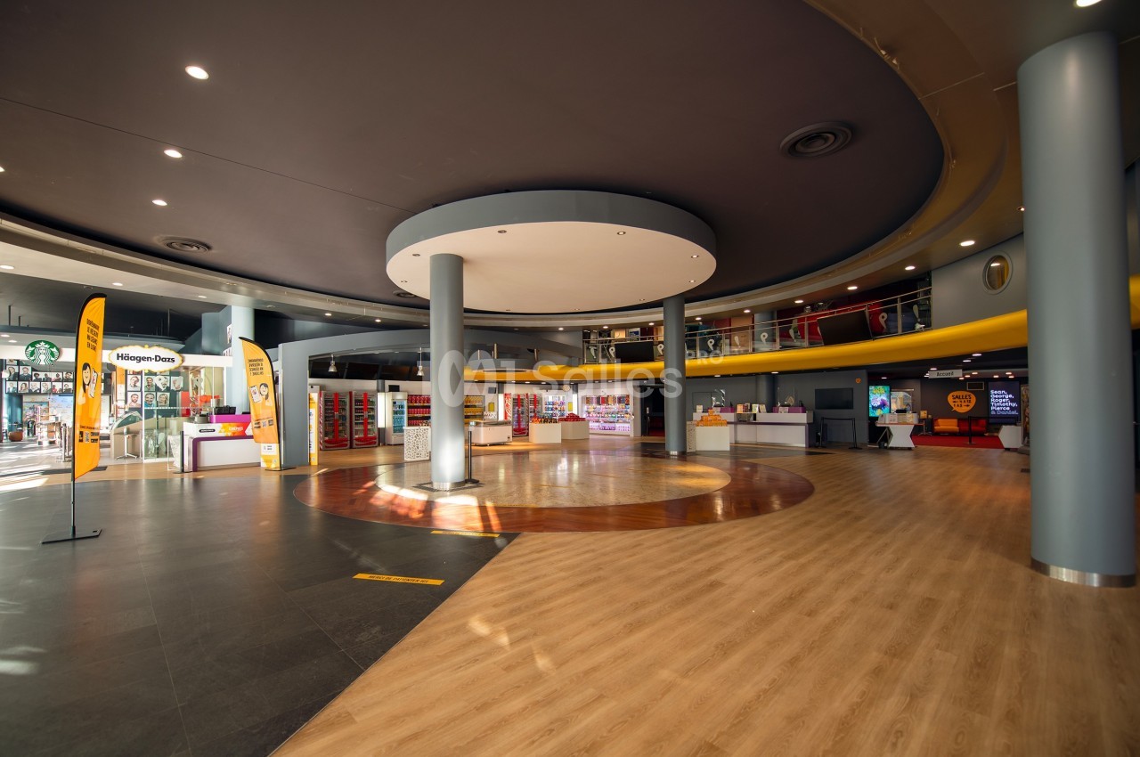 Intérieur spacieux d'un centre commercial avec un sol en bois et en carrelage, éclairage moderne et stands visibles.