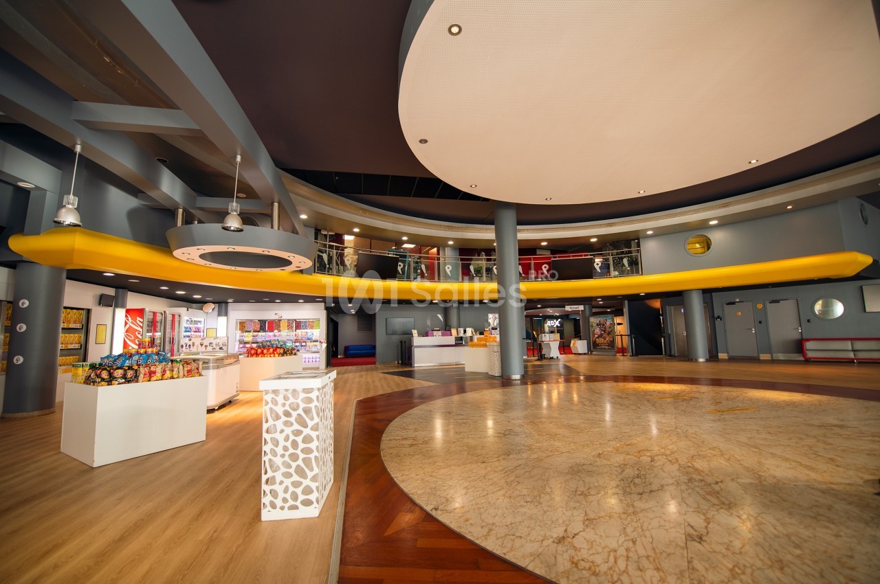 Hall spacieux avec sol en marbre, comptoirs modernes, mezzanine jaune et éclairage suspendu.