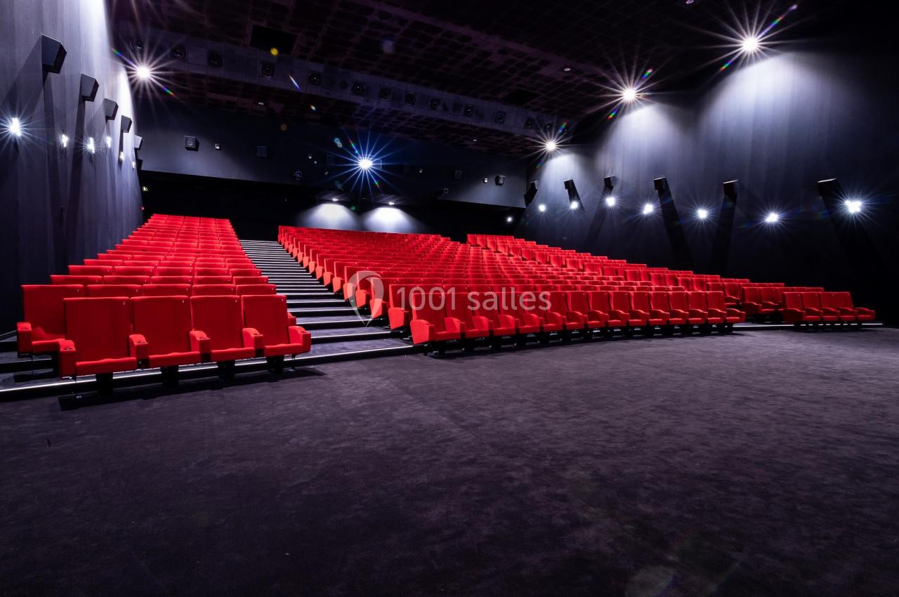 Salle de cinéma vide avec des rangées de sièges rouges et un éclairage tamisé.