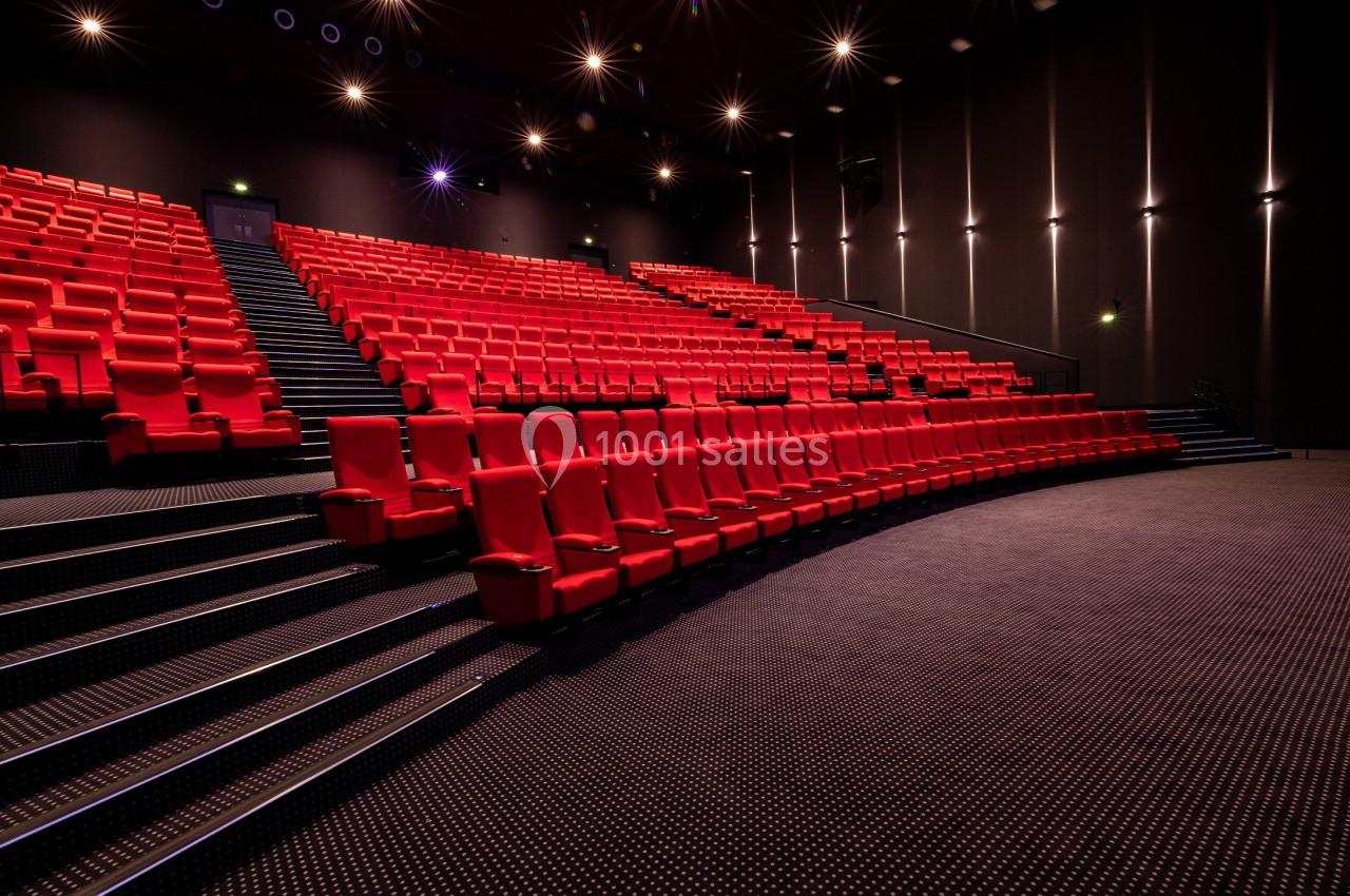 Salle de cinéma vide avec des rangées de fauteuils rouges et un éclairage tamisé.