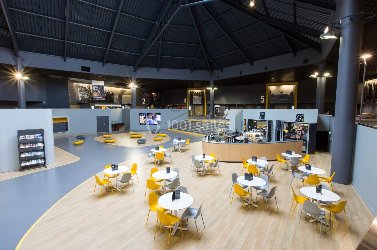 Salle spacieuse avec tables et chaises jaunes et grises, comptoir de café et numéros indiquant différentes sections.