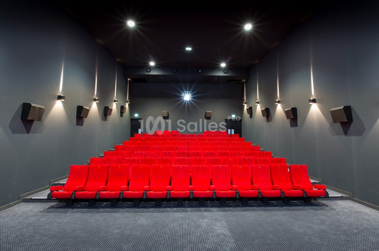 Salle de cinéma vide avec rangées de sièges rouges alignés et éclairage tamisé sur les murs gris.