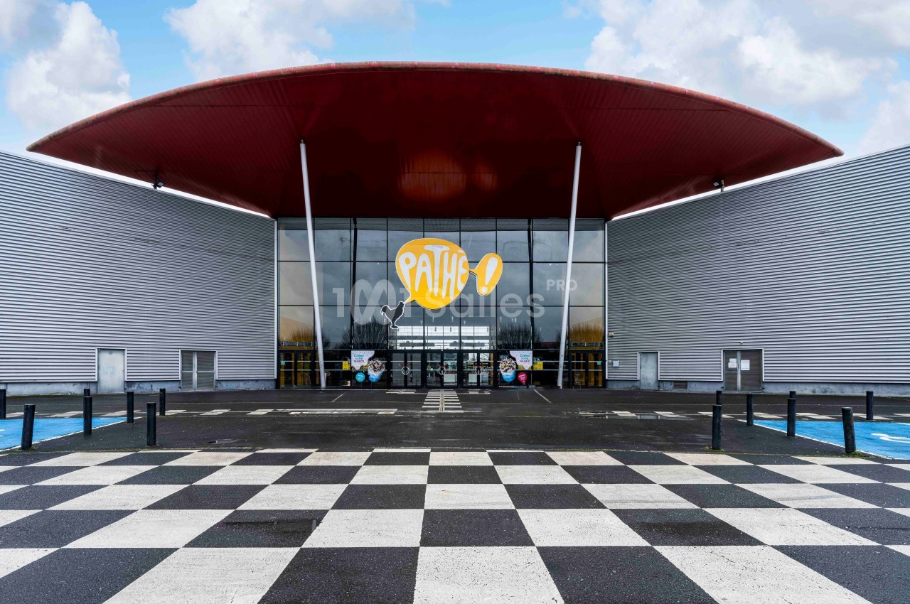 Façade d'un cinéma Pathé avec une entrée vitrée, un toit rouge et un sol à motifs en damier noir et blanc.