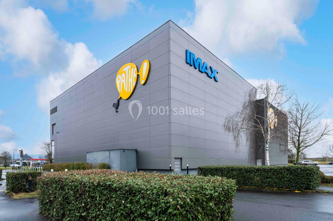 Façade d'un cinéma Pathé avec enseigne IMAX, entourée de haies et d'arbres sous un ciel nuageux.