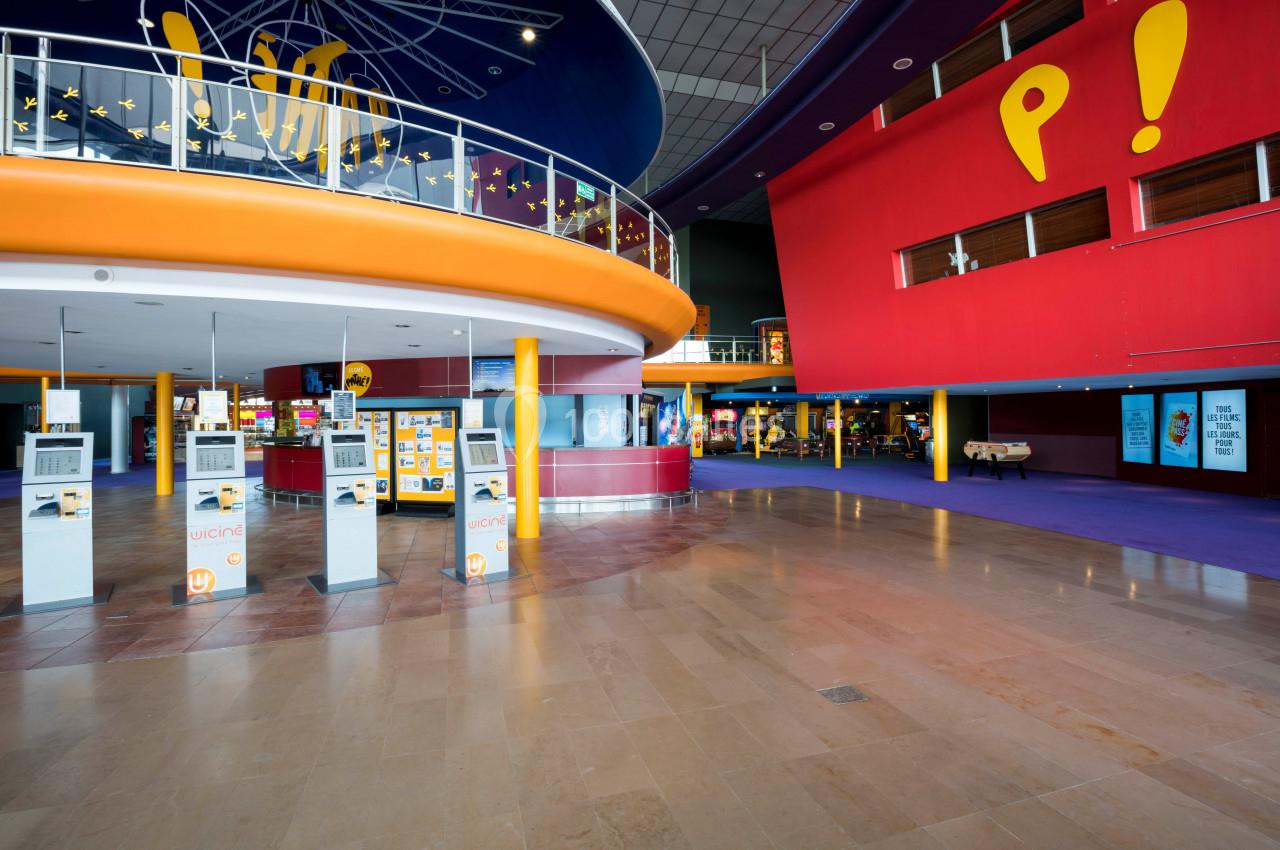 Hall spacieux d'un cinéma avec bornes automatiques, comptoirs de confiserie et décorations colorées.