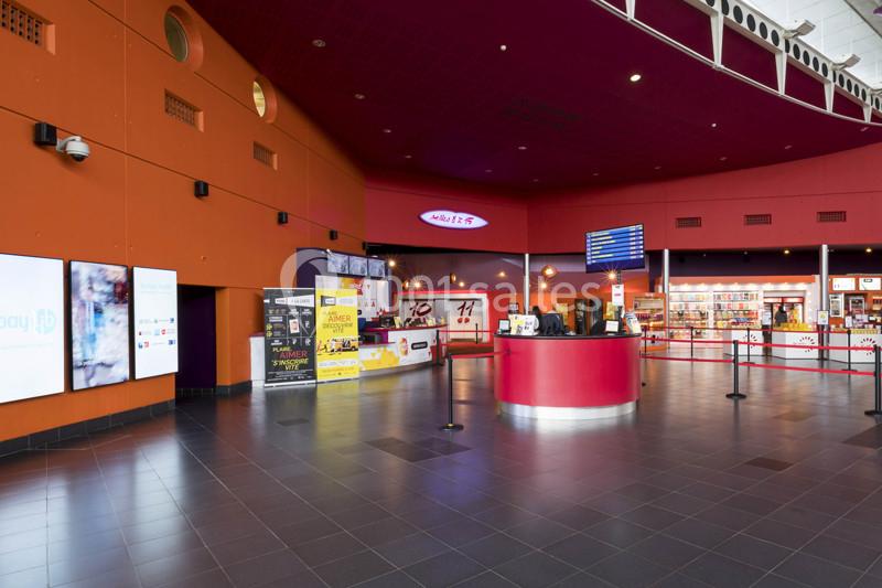 Hall d'entrée d'un cinéma avec un comptoir central, des affiches promotionnelles et un espace billetterie.