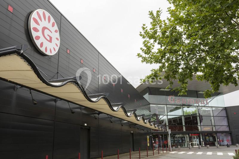 Façade d'un cinéma avec un logo circulaire et une entrée vitrée, entourée d'arbres et d'un ciel nuageux.