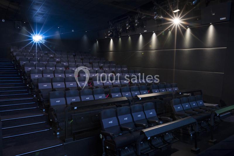 Salle de cinéma vide avec rangées de sièges inclinés et projecteurs allumés.