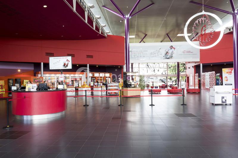 Hall d'entrée spacieux d'un cinéma avec comptoirs rouges, affiches, et éclairage moderne.