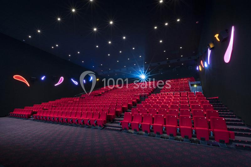 Salle de cinéma vide avec rangées de sièges rouges, éclairage tamisé et décorations lumineuses colorées sur les murs.
