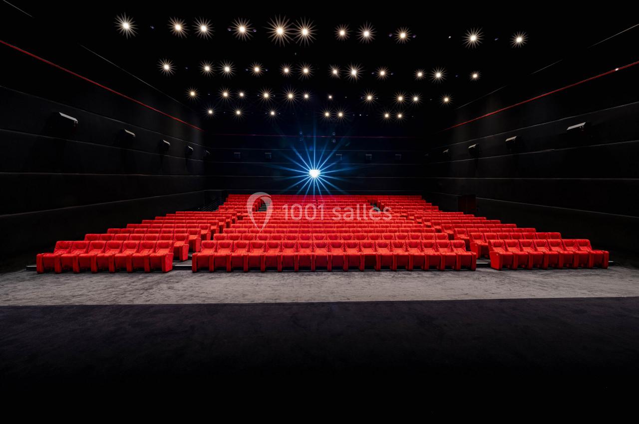 Salle de cinéma vide avec des rangées de sièges rouges et un projecteur allumé au fond.
