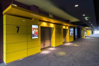 Miniature Location salle Coquelles (Pas-de-Calais) - Pathé Cité Europe #10 Couloir lumineux avec moquette grise, fauteuils, murs sombres, panneaux jaunes et ascenseurs numérotés 10.