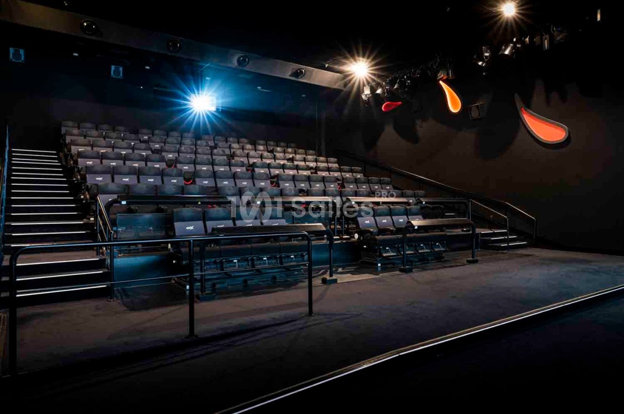 Salle de cinéma vide avec rangées de sièges, éclairage tamisé et projecteur allumé.