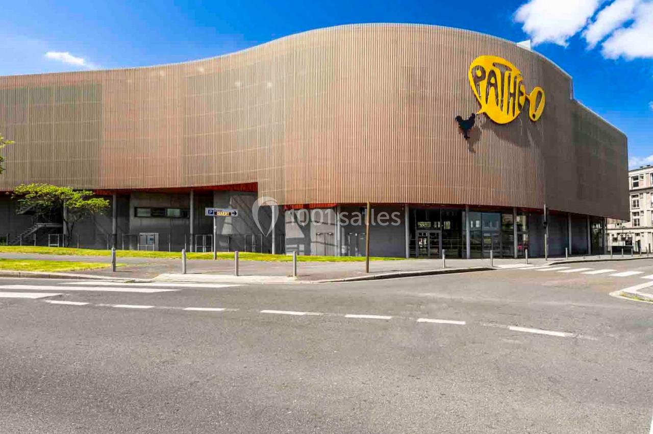 Façade d'un cinéma moderne avec un logo jaune ’Pathé’, vue depuis une rue calme par temps ensoleillé.