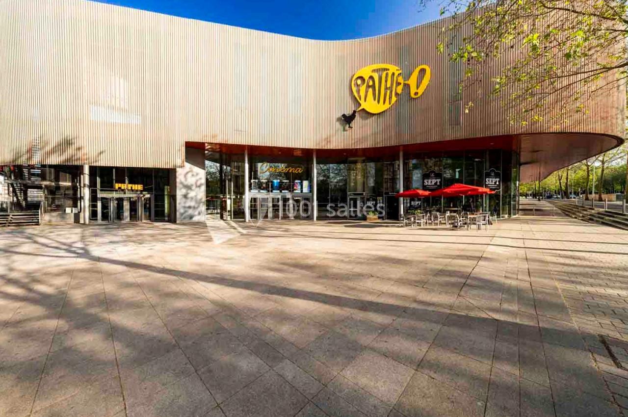 Façade d'un cinéma Pathé avec terrasse extérieure, parasols rouges et arbres en arrière-plan.