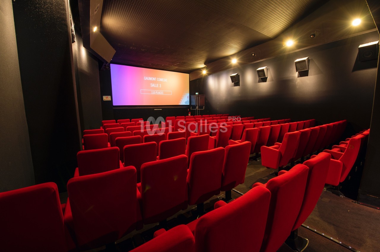 Salle de cinéma vide avec rangées de sièges rouges et écran allumé affichant des informations.