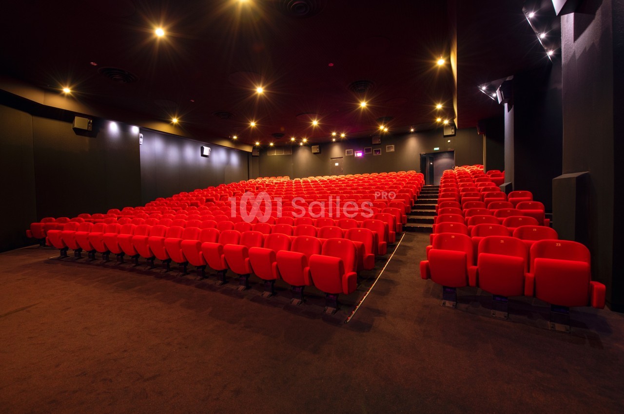 Salle de cinéma vide avec des rangées de sièges rouges et un éclairage tamisé.