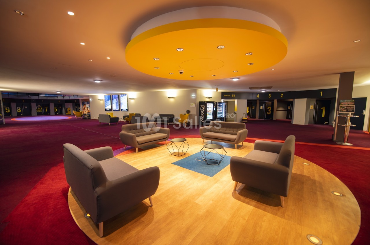 Espace d'attente moderne avec fauteuils gris, tables basses et éclairage circulaire jaune au plafond.