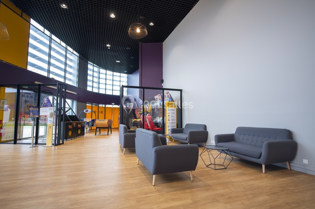 Espace d'accueil moderne avec canapés gris, tables basses et grandes baies vitrées laissant entrer la lumière naturelle.