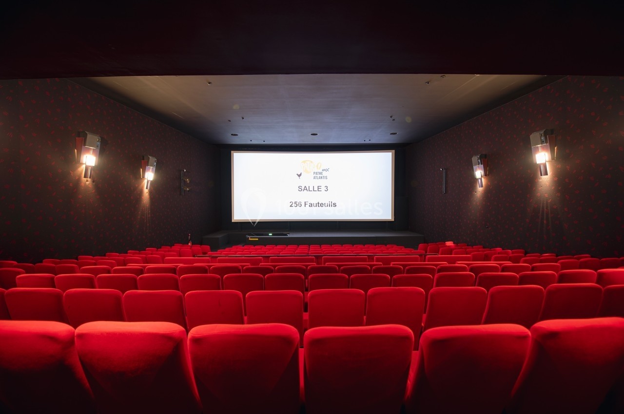Salle de cinéma vide avec des fauteuils rouges, écran affichant ’Salle 3, 256 fauteuils’ dans un décor sombre.