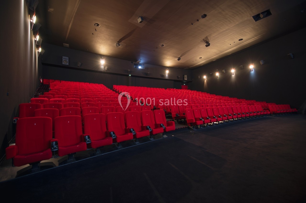 Salle de cinéma vide avec rangées de sièges rouges et éclairage tamisé.