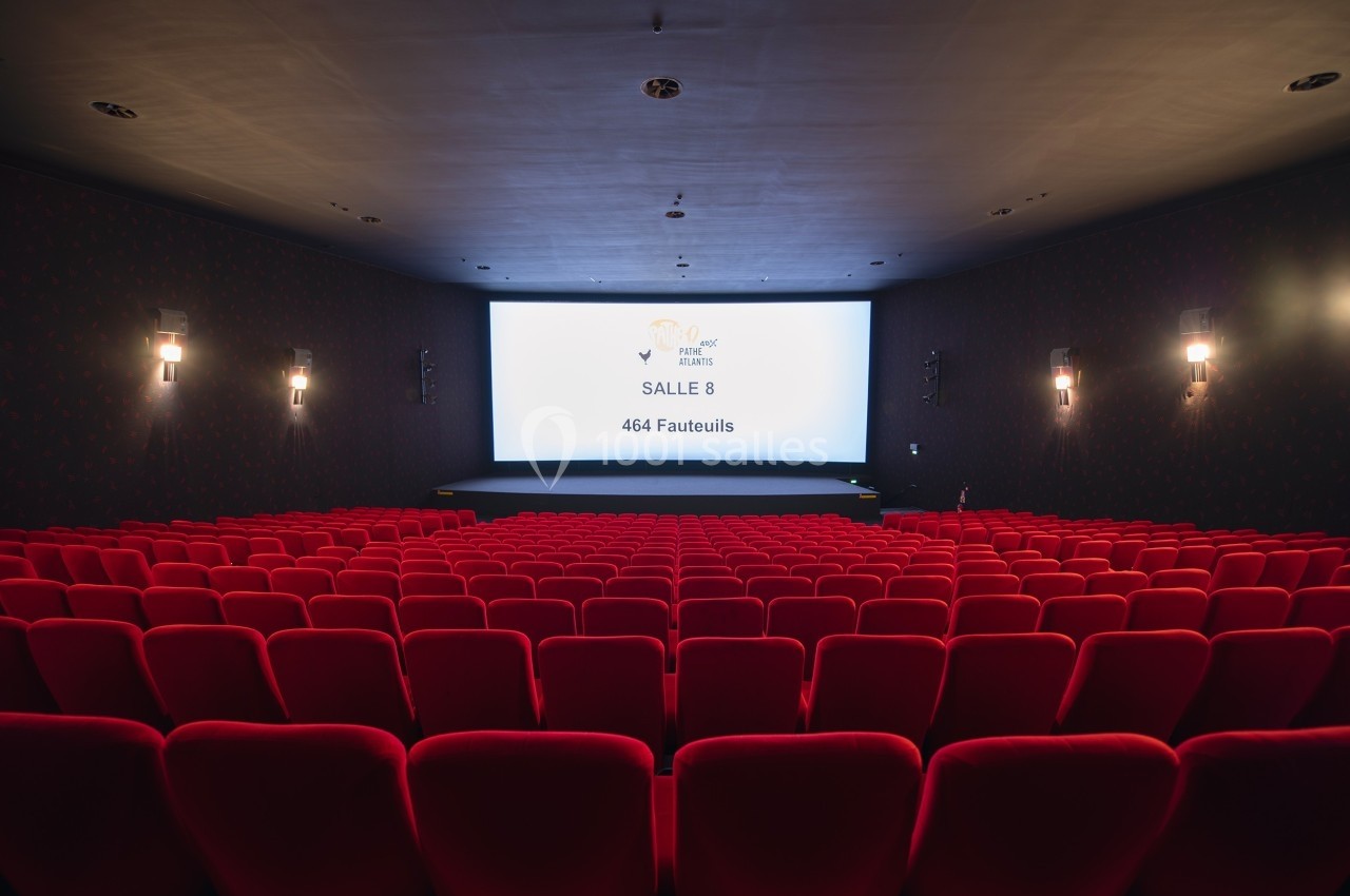 Salle de cinéma vide avec des rangées de fauteuils rouges et un écran affichant ’Salle 8, 464 fauteuils’.