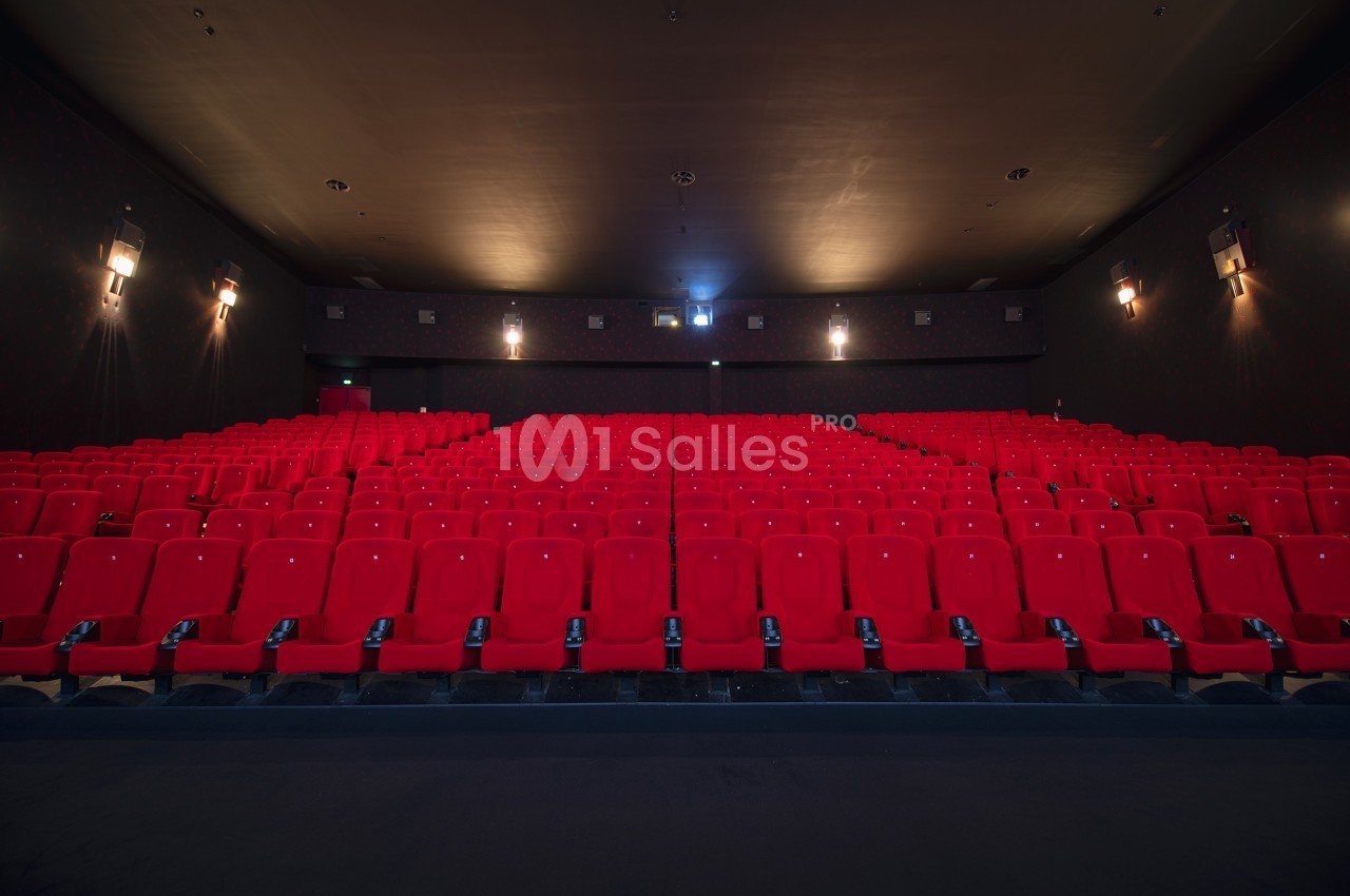 Salle de cinéma vide avec rangées de fauteuils rouges alignés face à un écran non visible.