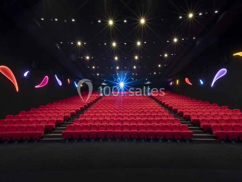 Salle de cinéma vide avec des rangées de sièges rouges, éclairage tamisé et décorations lumineuses colorées sur les murs.