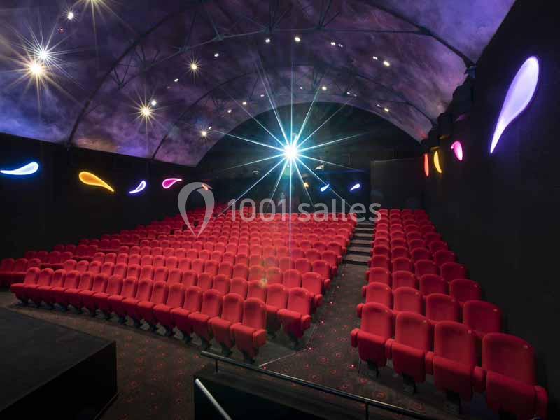 Salle de cinéma vide avec sièges rouges, éclairage tamisé et décorations lumineuses colorées sur les murs.