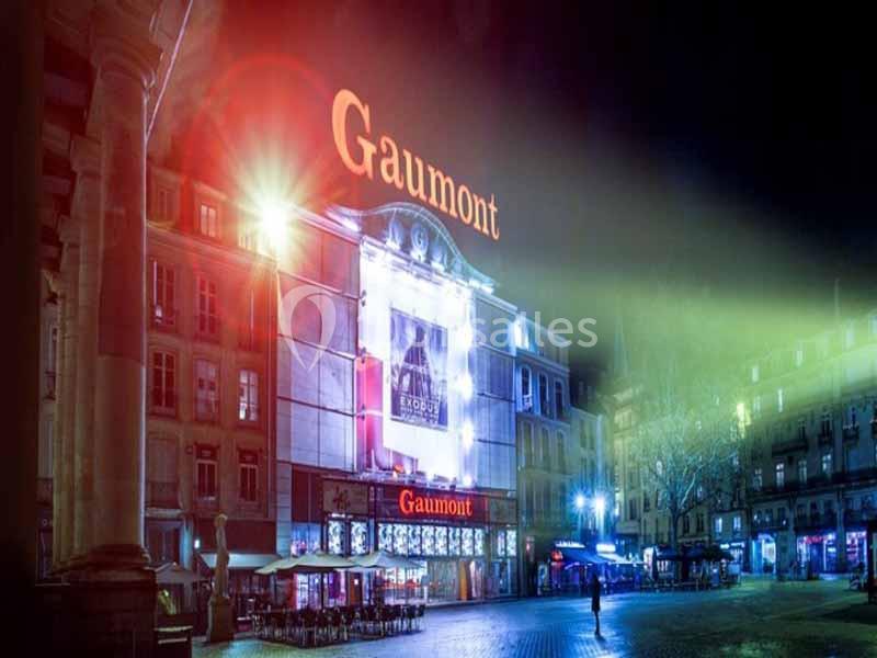 Façade illuminée d'un cinéma Gaumont la nuit, avec des enseignes lumineuses et une place déserte au premier plan.