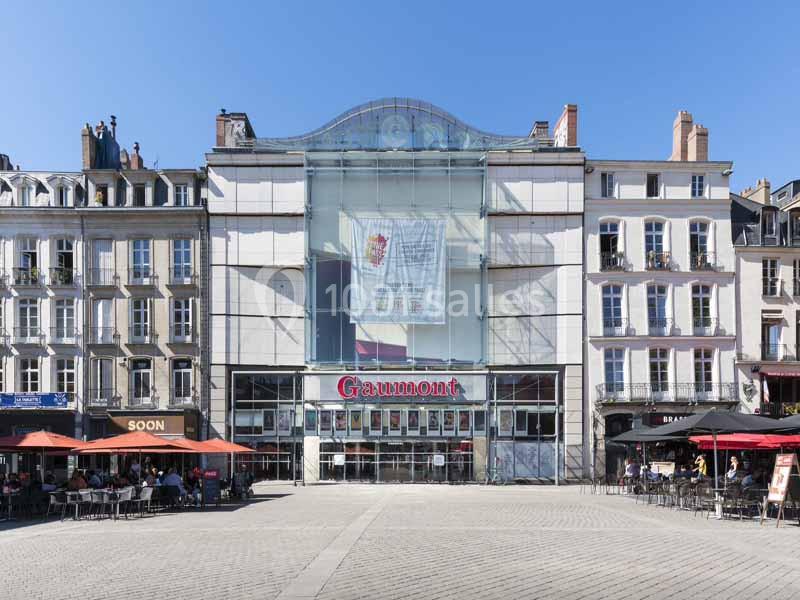Façade d'un cinéma Gaumont entouré de bâtiments anciens avec terrasses de cafés sur une place pavée.