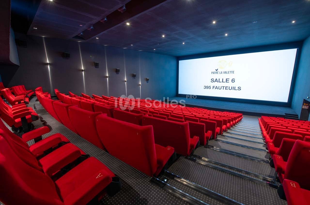 Salle de cinéma moderne avec des rangées de fauteuils rouges et un grand écran affichant des informations sur la salle.