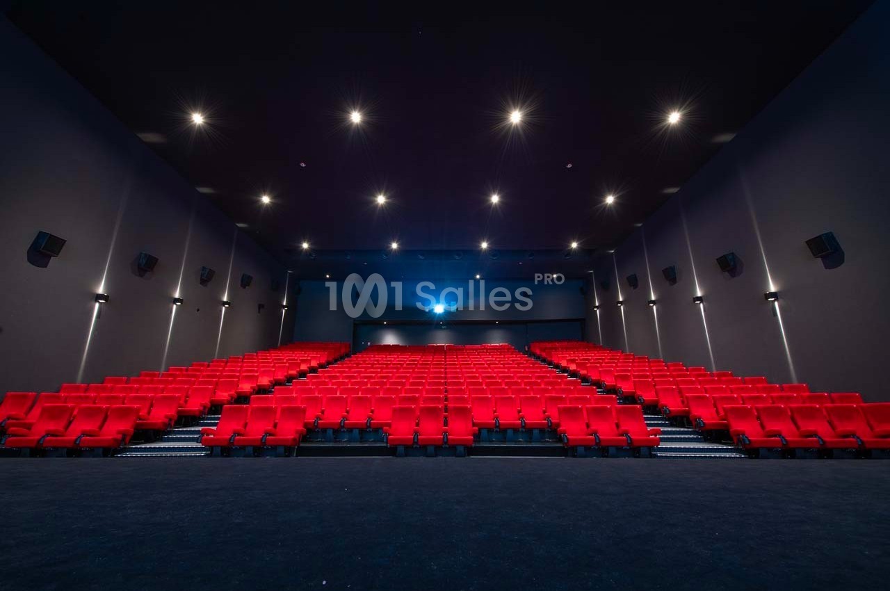 Salle de cinéma vide avec rangées de sièges rouges et éclairage tamisé au plafond.